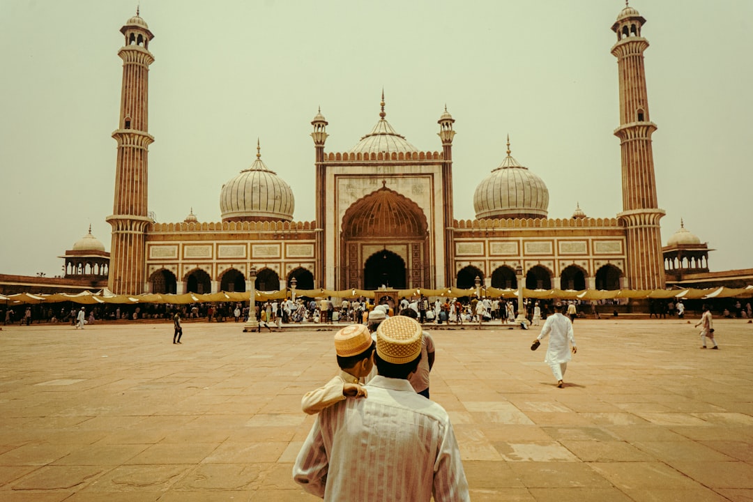 a-group-of-people-in-front-of-a-large-building-with-towers-with-jama-masjid-delhi-in-the-background-6ssltxygalg